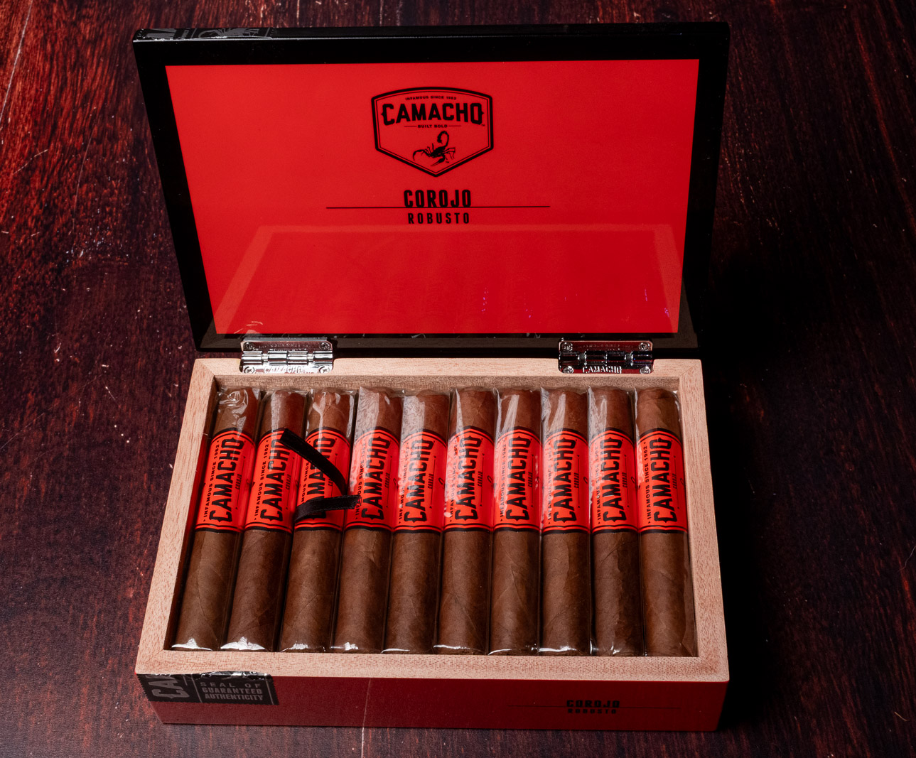 An open Camacho Corojo Robusto box with a red lid and a row of cigars wearing red and black bands