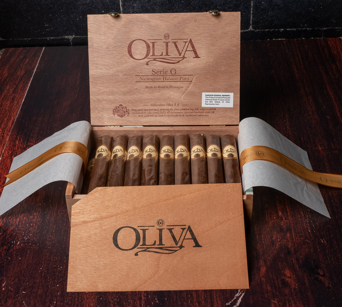 An open Oliva Serie O box with a row of banded robusto cigars and gold ribbon folded to either side