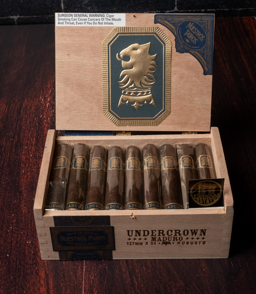 An open Undercrown Maduro Robusto box with a gold lion crest on the lid and dark maduro cigars inside