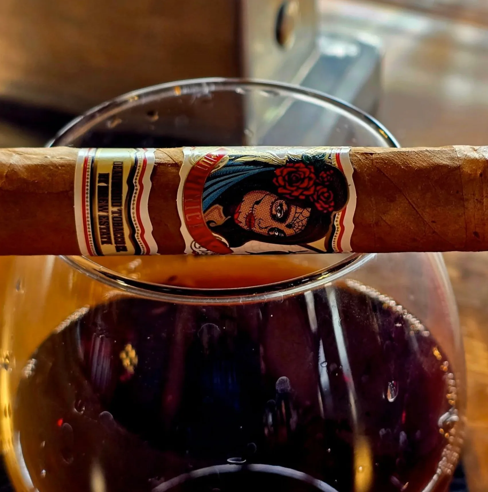 A cigar with an illustrated band resting across the rim of a glass